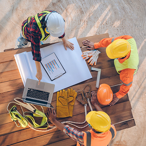 Overhead photo of a team of construction working engineers and architects, meeting, discussing, designing, planning, and measuring layouts of building blueprints at a construction site.