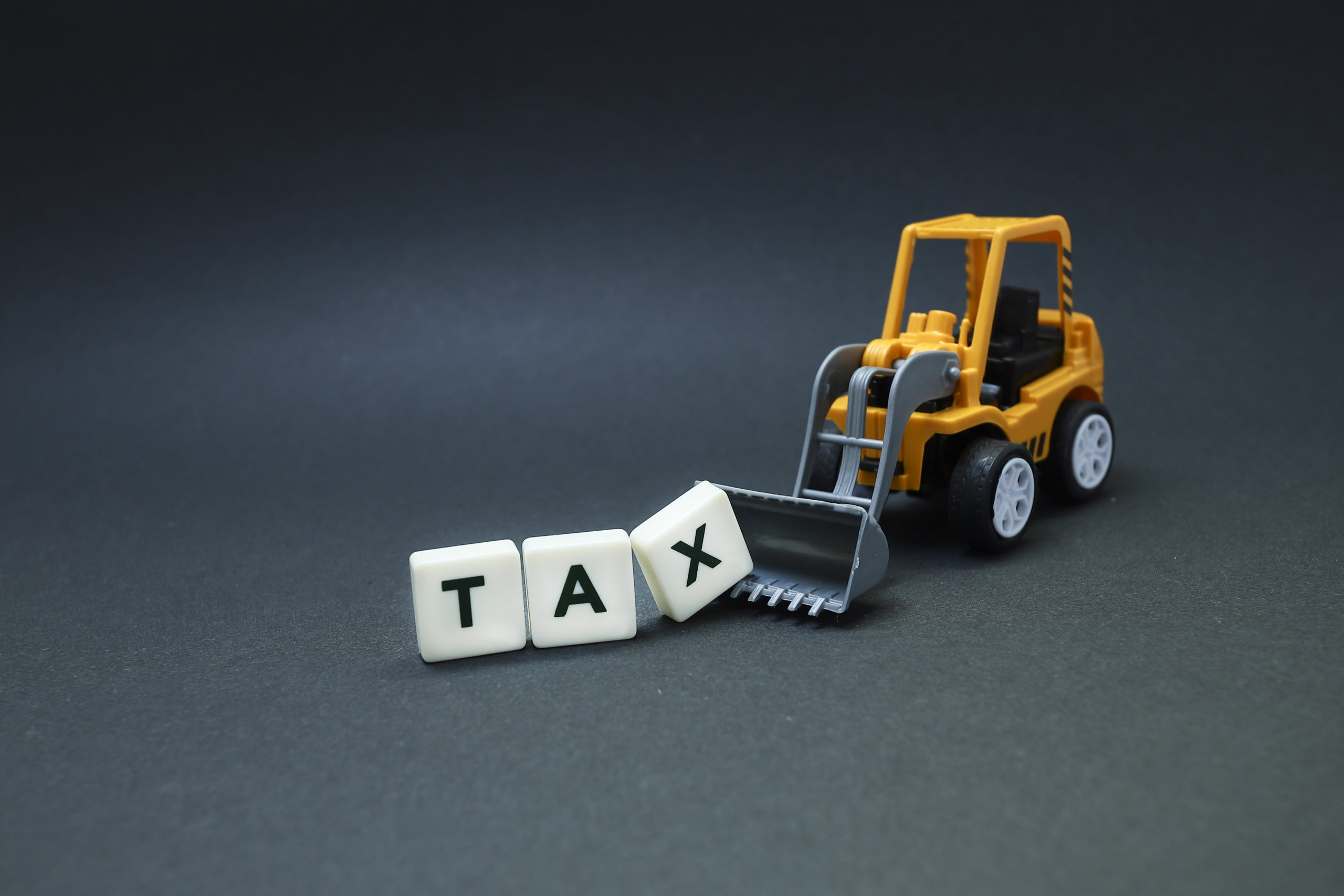 A macro photo of letter blocks spelling "TAX" being lifted by a bulldozer