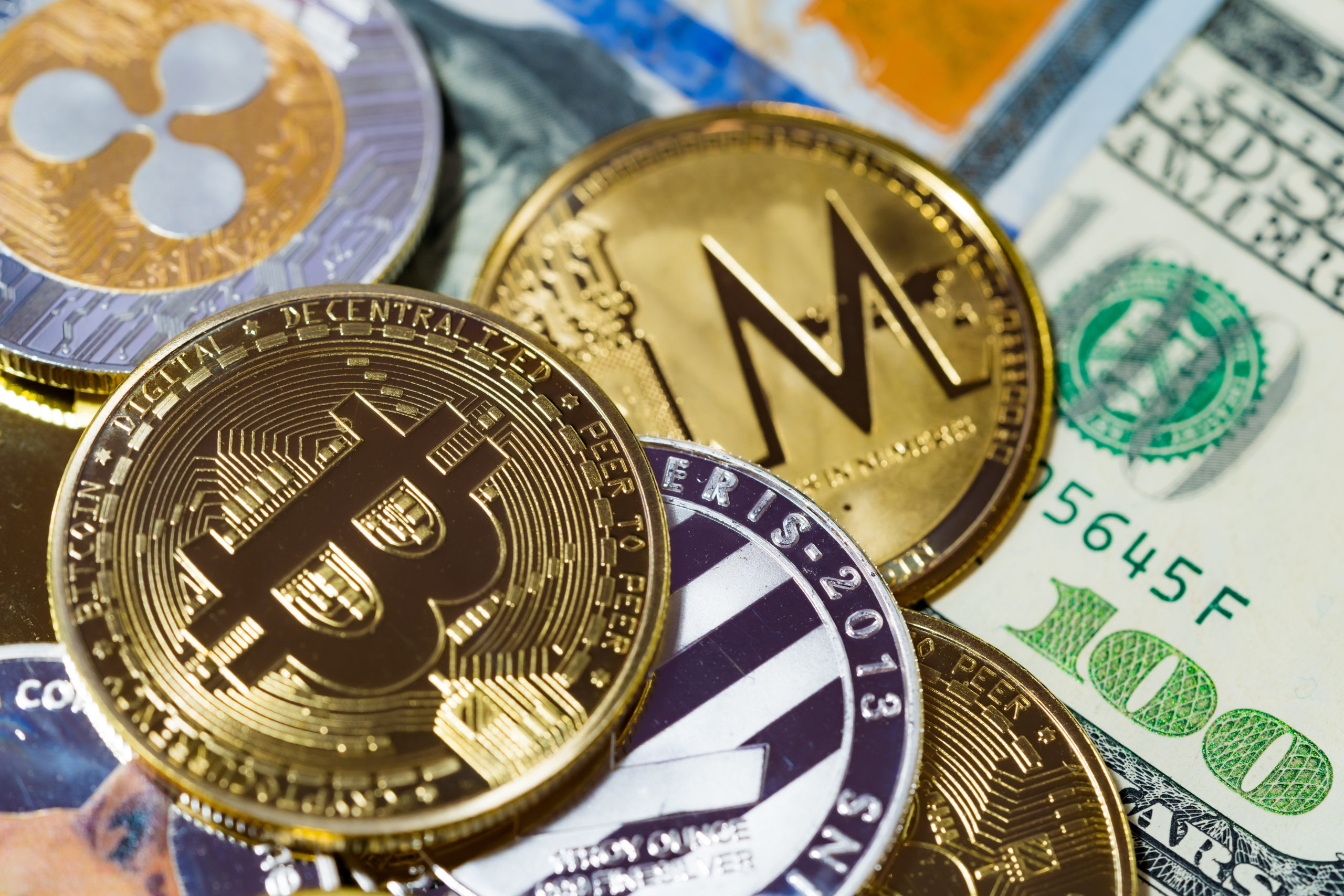 Photo of physical coins depicting different types of cryptocurrencies, on top of a $100 bill